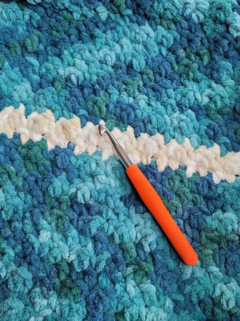 Chunky yarn blanket in ocean inspired colors (blues and greens) with white stripes.