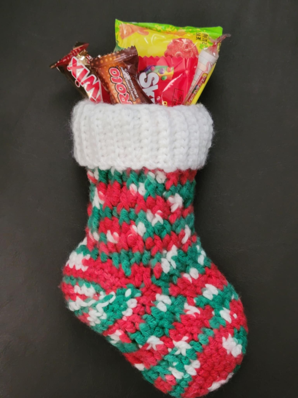Medium sized holiday stocking in festive red, green, and white yarn with a white cuff with candy inside