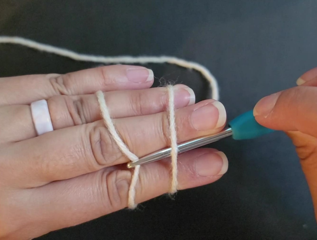 picture of back of hand with 2 parallel yarn strands showing and the crochet hook under the first strand closest to the finger tips and grabbing the second strand to pull through