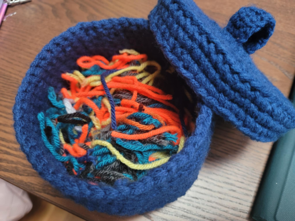 blue tabletop scrap bin with lid that has multiple bits of scrap yarn inside of different colors.