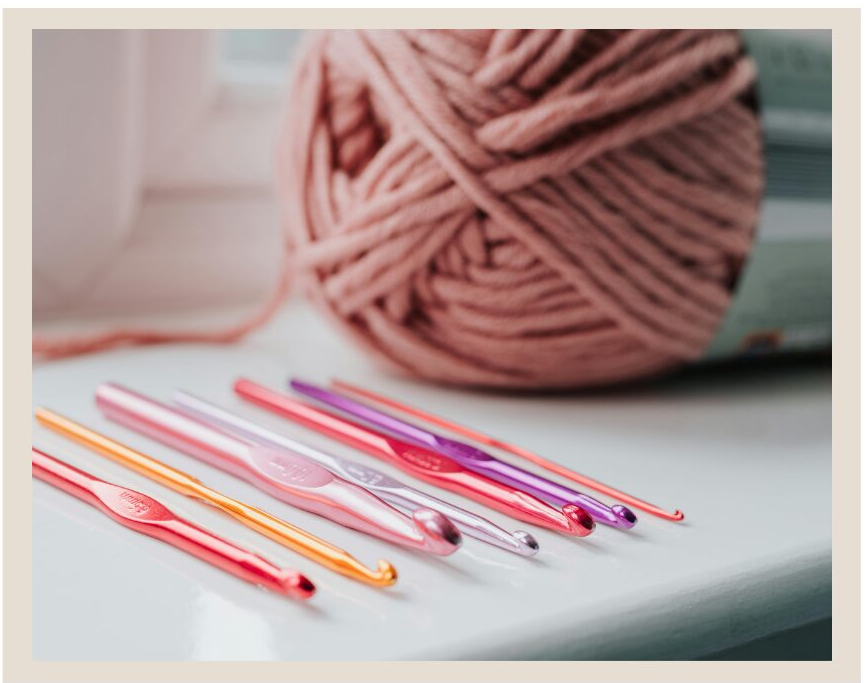 picture of a pink skein of yarn with 7 multiple sized crochet hooks in different colors in front of it